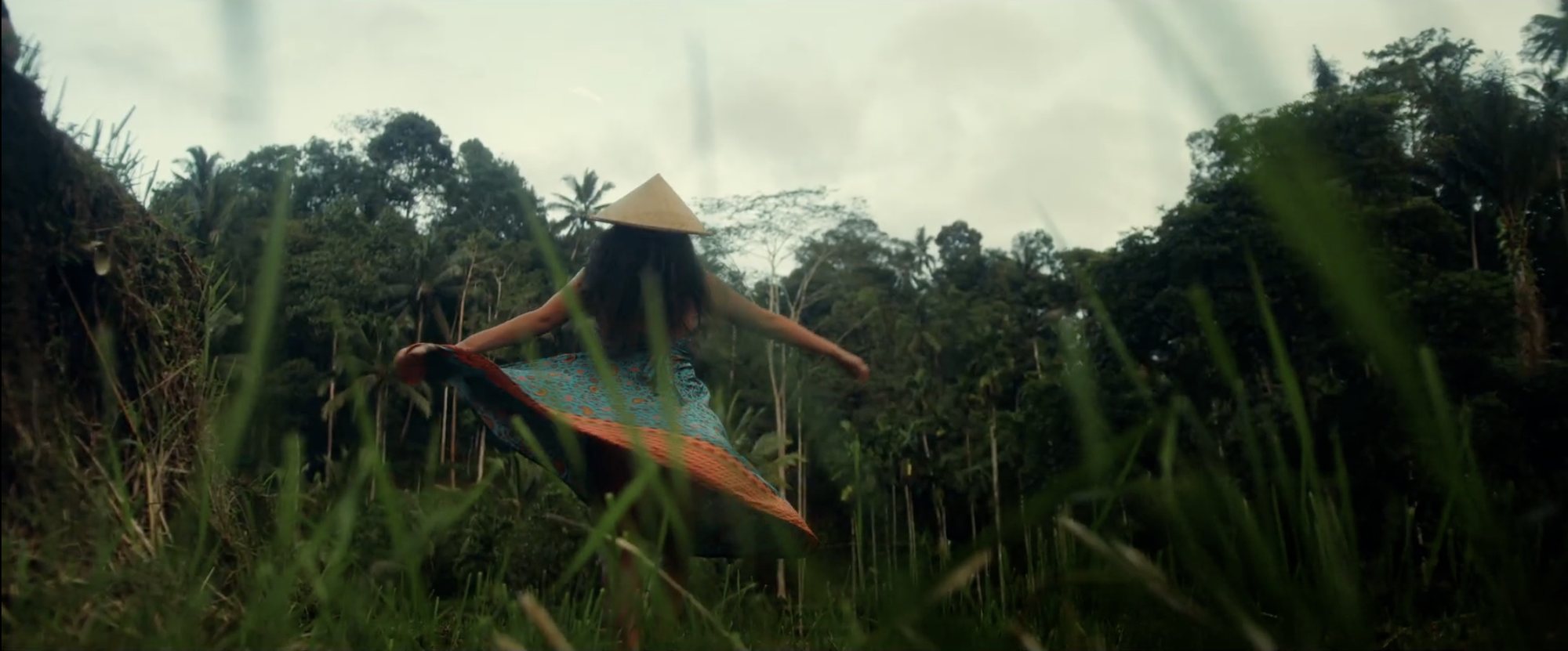 Maria twirling in a patterned skirt among tall grass and palms in Bali