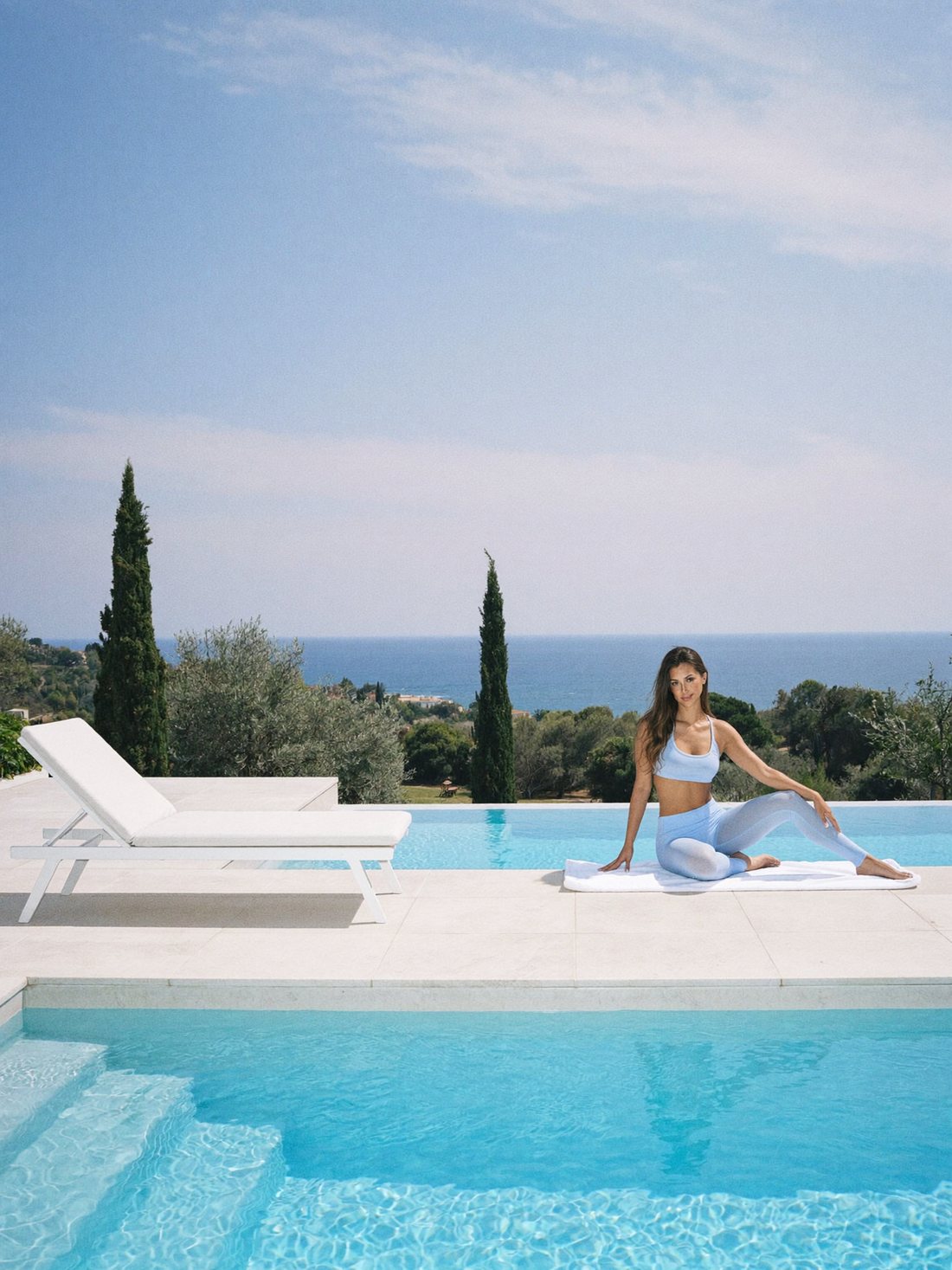 Maria stretching on a towel at the edge of an infinity pool overlooking the sea