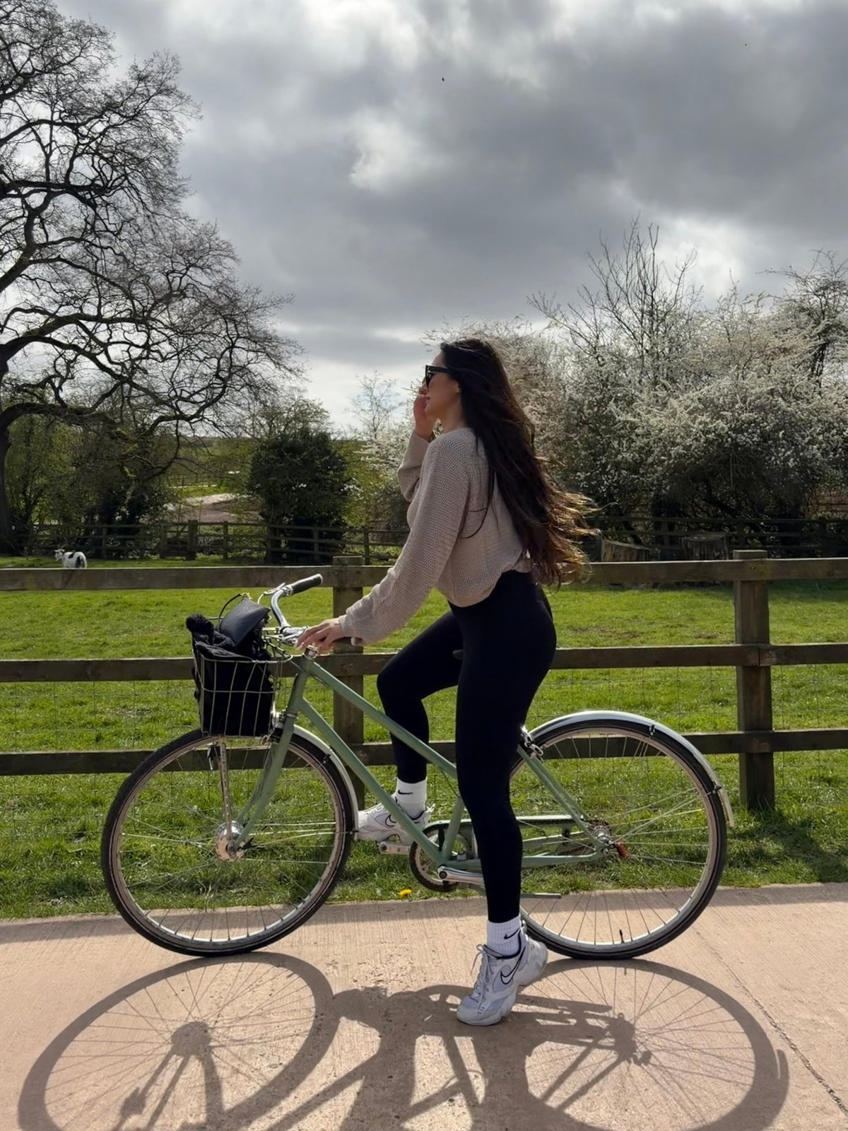Maria on a green bicycle with a basket beside a countryside field
